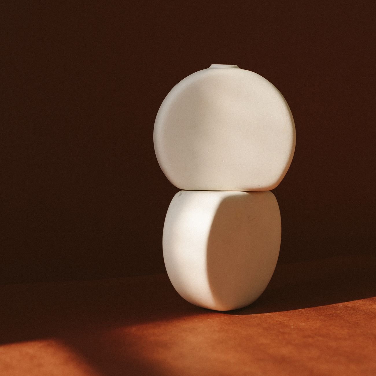 Elegant ceramic vase with minimalist design highlighted by warm sunlight against a brown background.